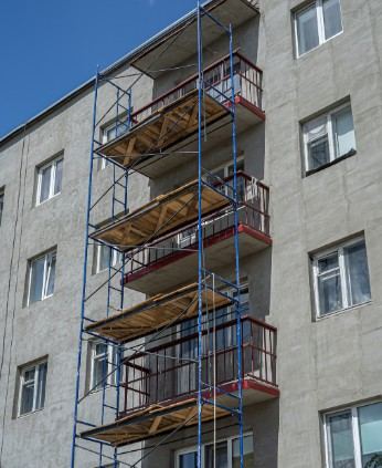 Rehabilitación de fachada de bloques en Mallorca Andamio metálico con plataformas de madera ante un bloque de viviendas: andamio de obra en edificio habitado