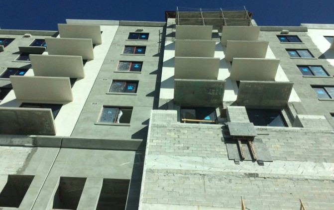 Edificio de viviendas en obra visto desde abajo, con balcones de paneles claros y fachada gris: obra de envolvente térmica