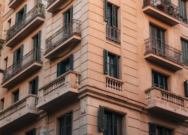 Edificio de viviendas color terracota con balcones de forja y balaustradas en esquina: fachada de edificio de ensanche