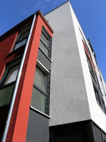 Esquina de un edificio con revestimiento rojo y gris y carpintería oscura: acabado de fachada en rojo y gris en Llucmajor