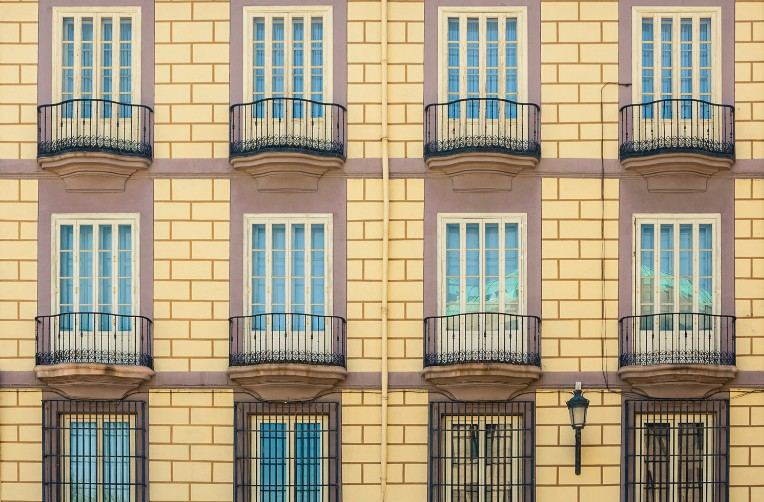 Fachada amarilla de edificio con balcones de forja y ventanas con persiana: fachada de ensanche con balcones