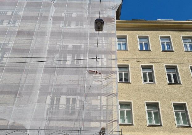 Fachada cubierta por la malla del andamio junto a un edificio ya rehabilitado: protección de la vía pública en obra
