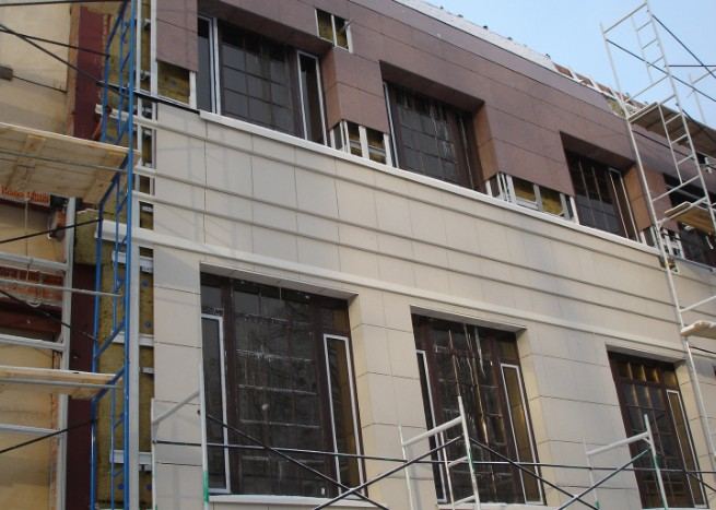 Revestimiento de fachada con paneles en Mallorca Fachada ventilada en montaje, con paneles claros y andamio sobre ventanas oscuras: fachada ventilada con paneles