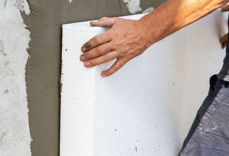 Aislamiento de fachada por el exterior en Mallorca Mano colocando una placa de poliestireno expandido sobre el mortero adhesivo: mortero adhesivo para aislamiento