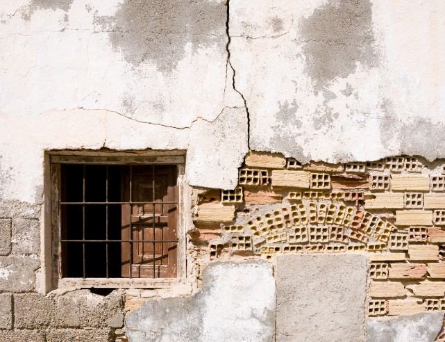 Desprendimiento de revoco en fachada en Mallorca Muro con el revoco desprendido que deja ver el ladrillo hueco junto a una ventana enrejada: patología de desprendimientos