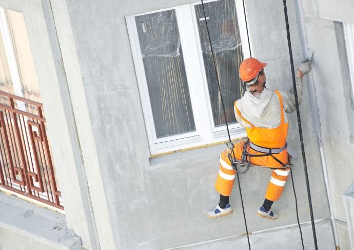 Acceso por cuerda sin andamio en Mallorca Operario con mono naranja descolgado por cuerda junto a una ventana: trabajos verticales en fachadas