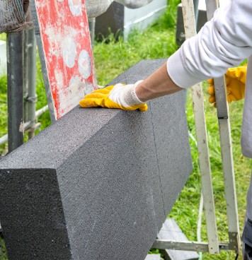Operario con guantes colocando una placa de aislante gris de grafito junto al andamio: colocación de placas de aislamiento