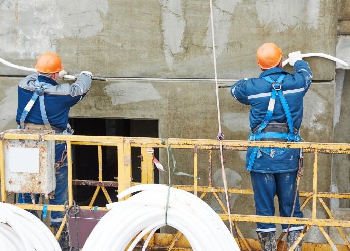 Dos operarios en una plataforma de trabajo amarilla sobre un paramento saneado: trabajos de fachada en altura