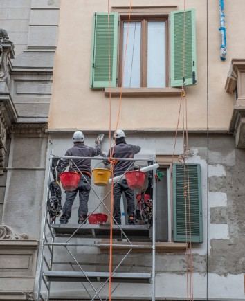 Dos operarios en una plataforma suspendida reparando la fachada de un edificio antiguo: plataforma suspendida para fachadas