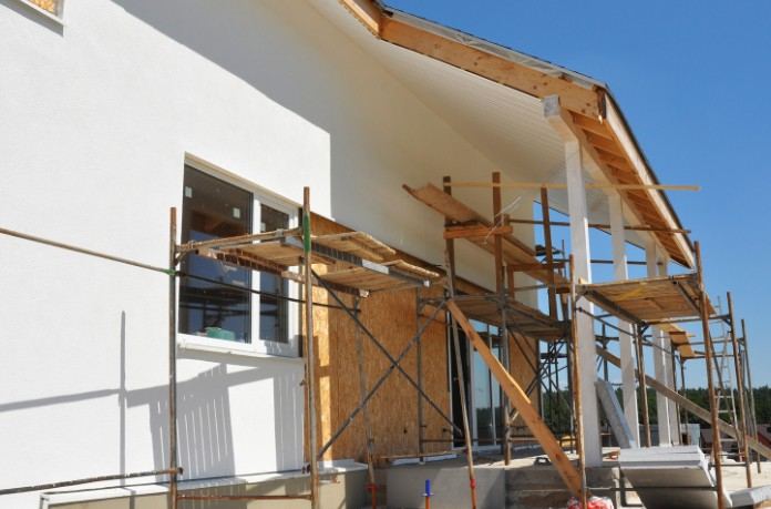 Vivienda de fachada blanca recién revocada con andamio de madera y cielo azul: reforma exterior de un chalet